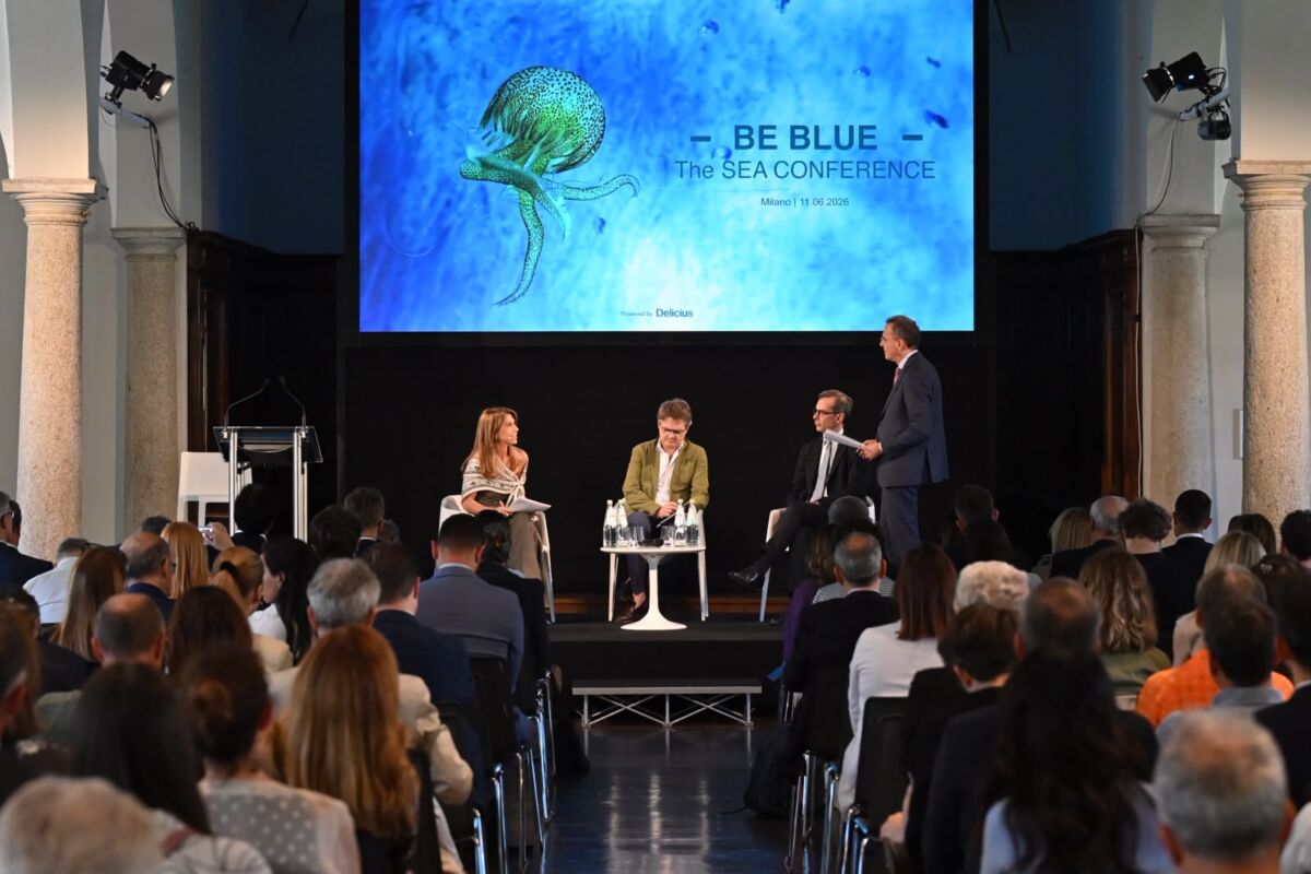 Conferenza Blue Economy a Milano: relatori sul palco davanti a uno schermo con logo Be Blue e immagine di una medusa.