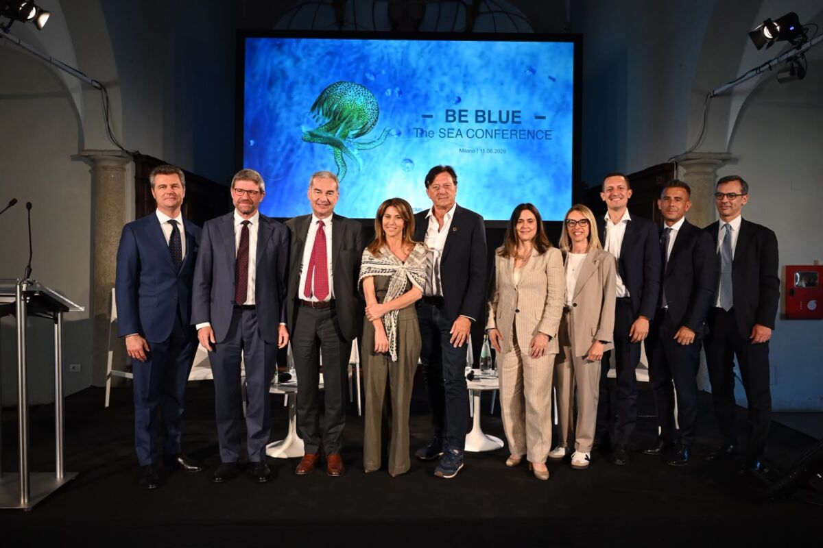 Gruppo di relatori sul palco della conferenza Blue Economy a Milano davanti allo schermo con logo Be Blue The Sea.