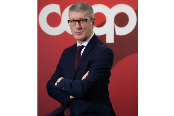 Domenico Brisigotti, Presidente di Coop Italia, in posa professionale davanti al logo aziendale su sfondo rosso.