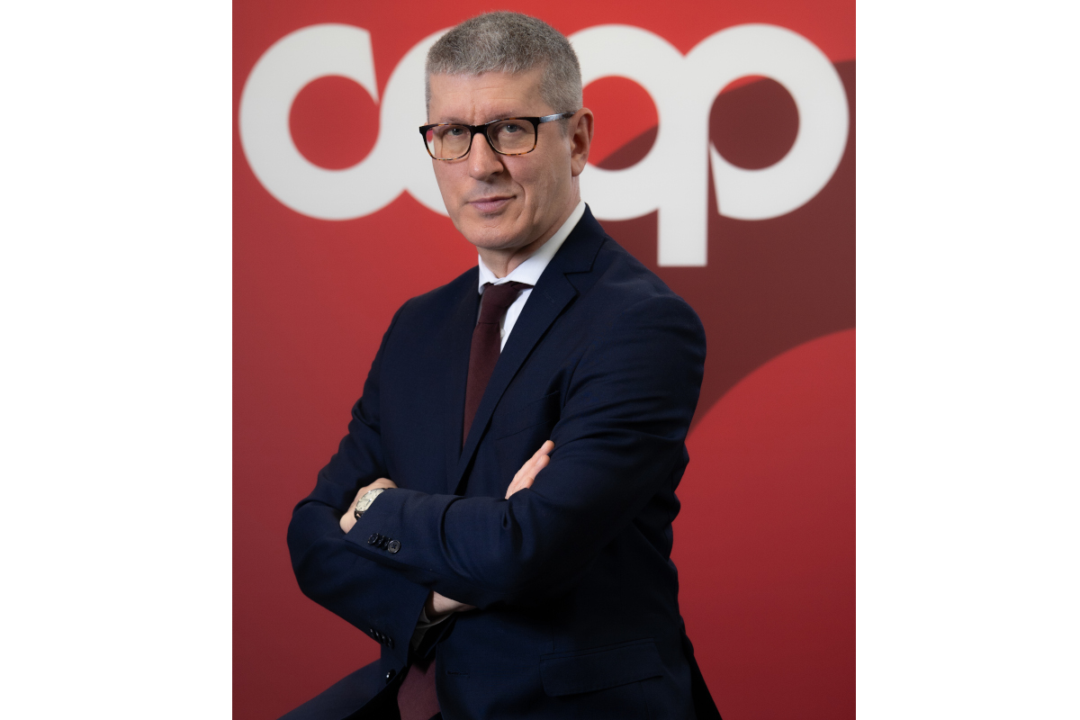 Domenico Brisigotti, Presidente di Coop Italia, in posa professionale davanti al logo aziendale su sfondo rosso.