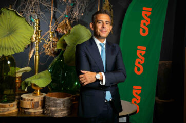 Giangiacomo Ibba, presidente di Crai Secom, in giacca e cravatta davanti a una bandiera verde con logo Crai.