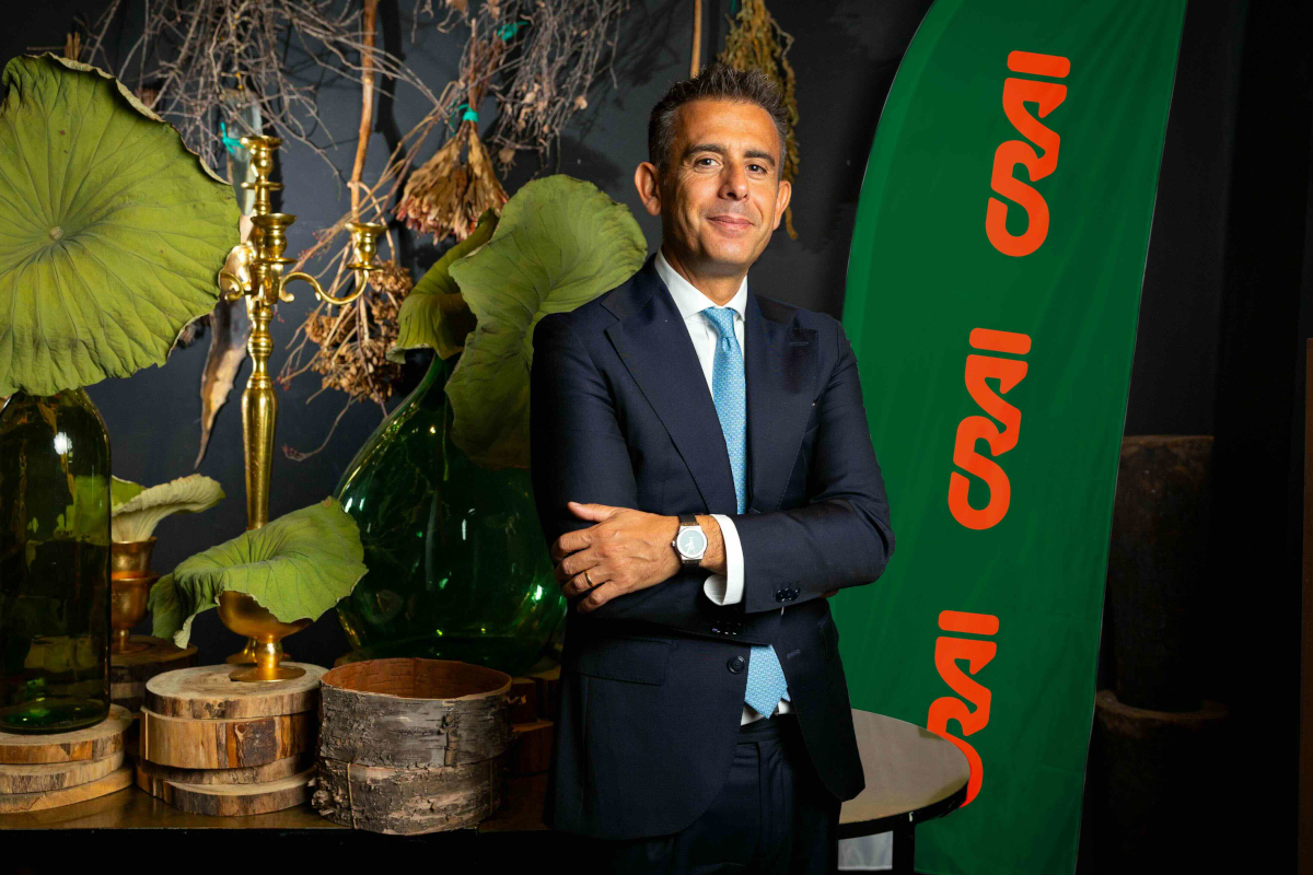 Giangiacomo Ibba, presidente di Crai Secom, in giacca e cravatta davanti a una bandiera verde con logo Crai.