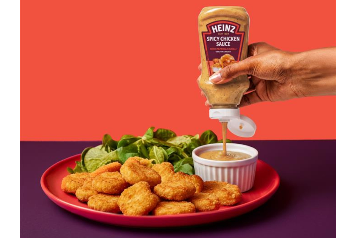 Mano che versa la nuova salsa Heinz Spicy Chicken su un piatto di croccanti bocconcini di pollo con insalata fresca.