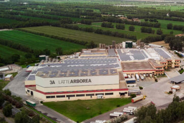Veduta aerea dello stabilimento 3A Latte Arborea in Sardegna, con pannelli solari sul tetto e camion nel piazzale.