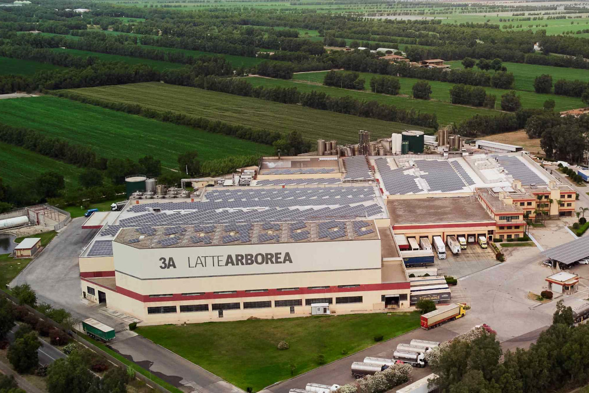 Veduta aerea dello stabilimento 3A Latte Arborea in Sardegna, con pannelli solari sul tetto e camion nel piazzale.