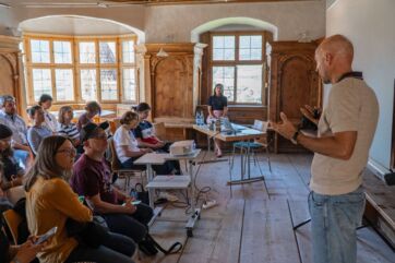 Relatore tiene una presentazione sulle mele della Val Venosta davanti a un pubblico in una sala storica in legno.