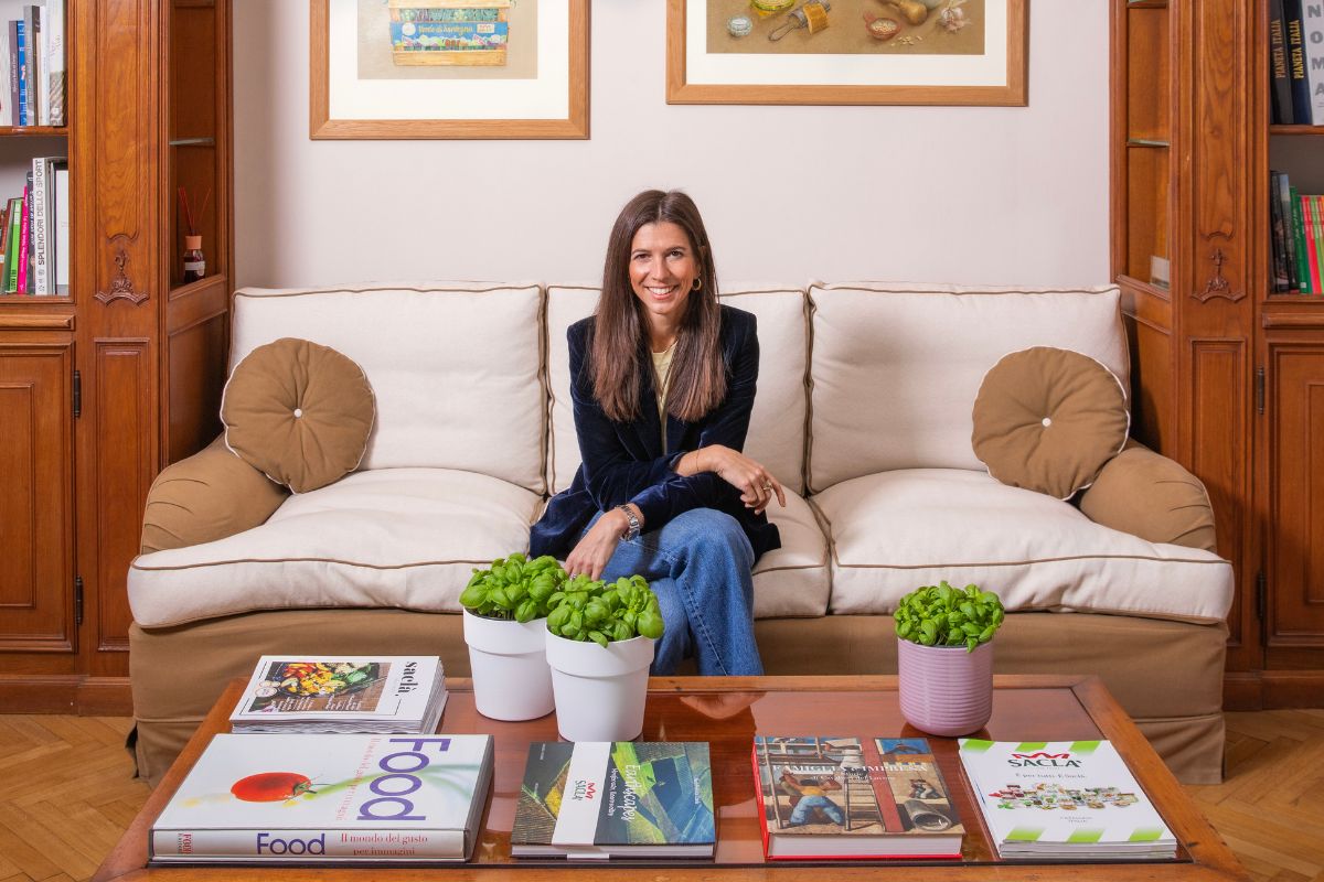 Chiara Ercole, CEO di F.lli Saclà, seduta sul divano in un ufficio elegante con libri e piante di basilico sul tavolo.
