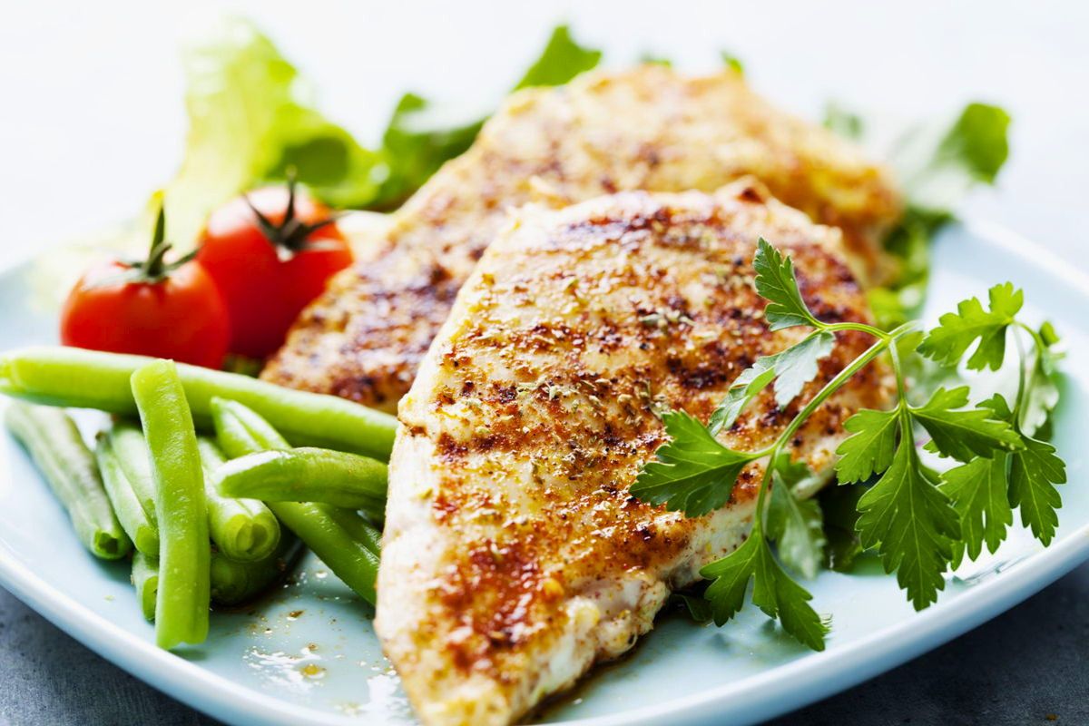 Petto di pollo grigliato con fagiolini, pomodorini e prezzemolo, un piatto sano della filiera avicola italiana.