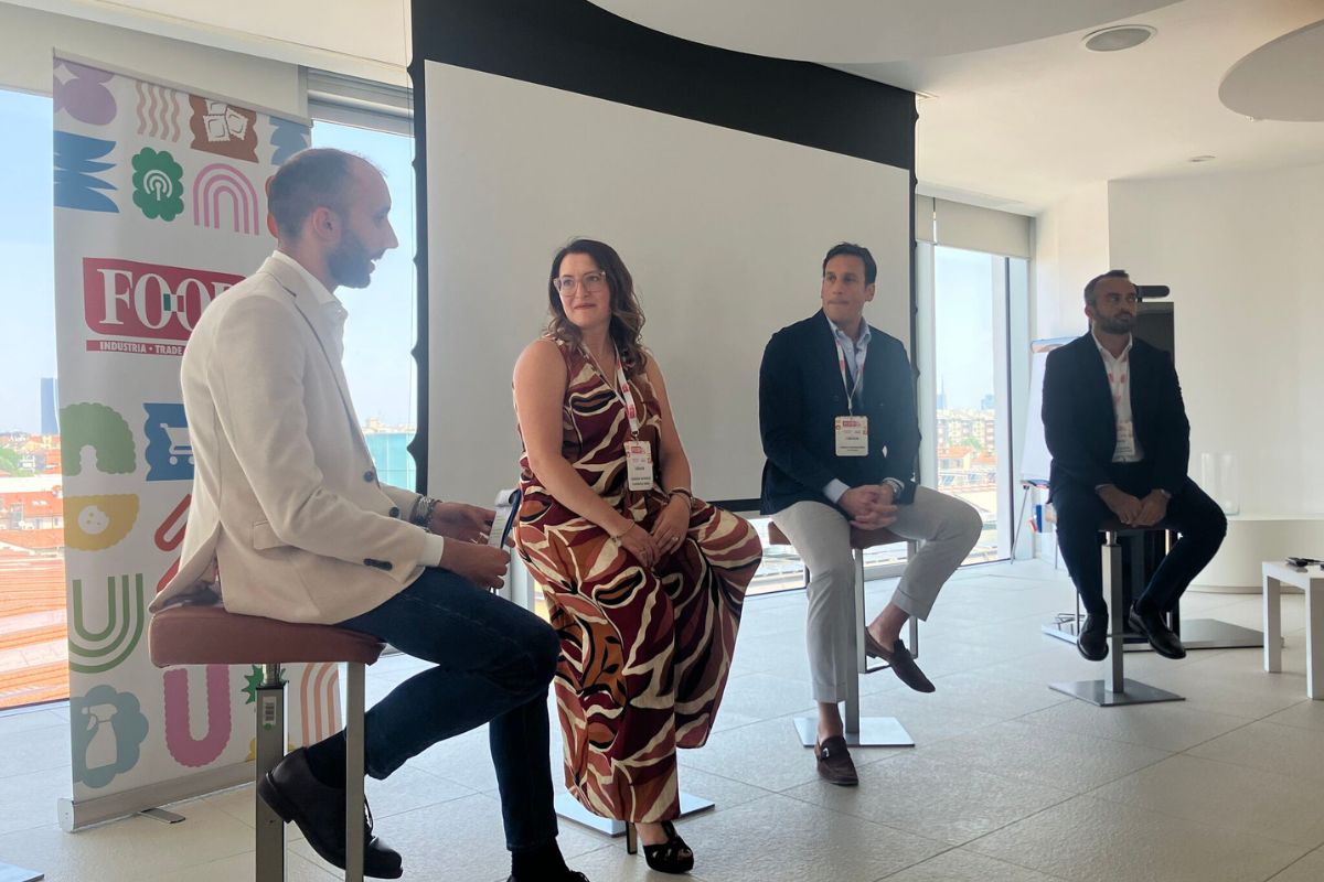 Relatori a un convegno sull'evoluzione dell'aperitivo e strategie di mixology, seduti su sgabelli in un ufficio moderno.