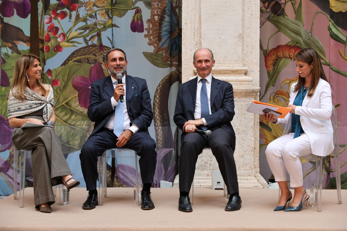 Conferenza per i 20 anni di Italia del Gusto con relatori su un palco davanti a un fondale botanico decorativo.
