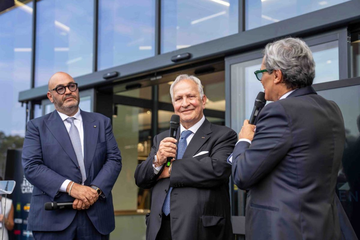 Inaugurazione de L’Arena di Catania: tre uomini in abito formale parlano al microfono davanti al nuovo hub sostenibile.