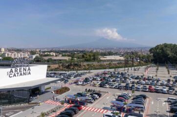 Veduta panoramica de L'Arena di Catania con ampio parcheggio e l'Etna sullo sfondo, hub di food experience e sostenibilità.