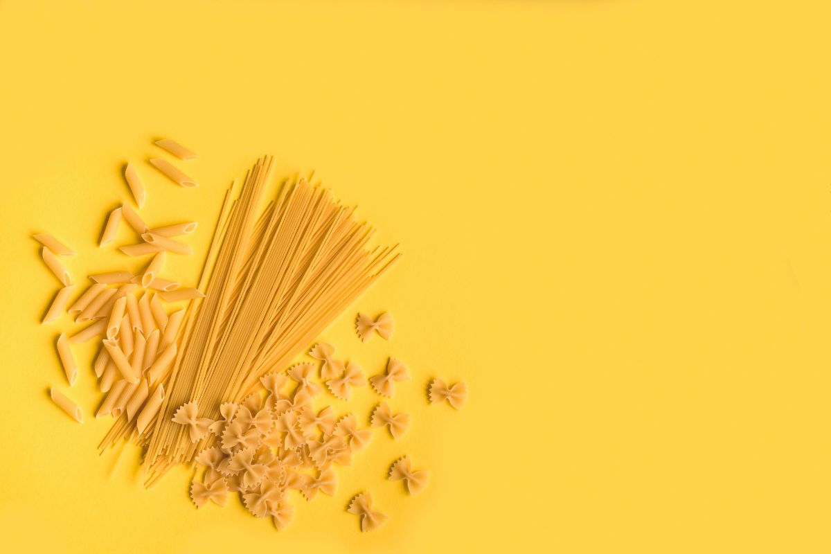 Spaghetti, penne e farfalle di pasta secca disposte su uno sfondo giallo brillante per un piatto di pasta creativo.