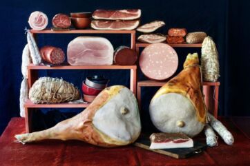 Selezione di pregiati salumi italiani, prosciutti crudi e mortadella esposti su scaffali per l'export gastronomico.