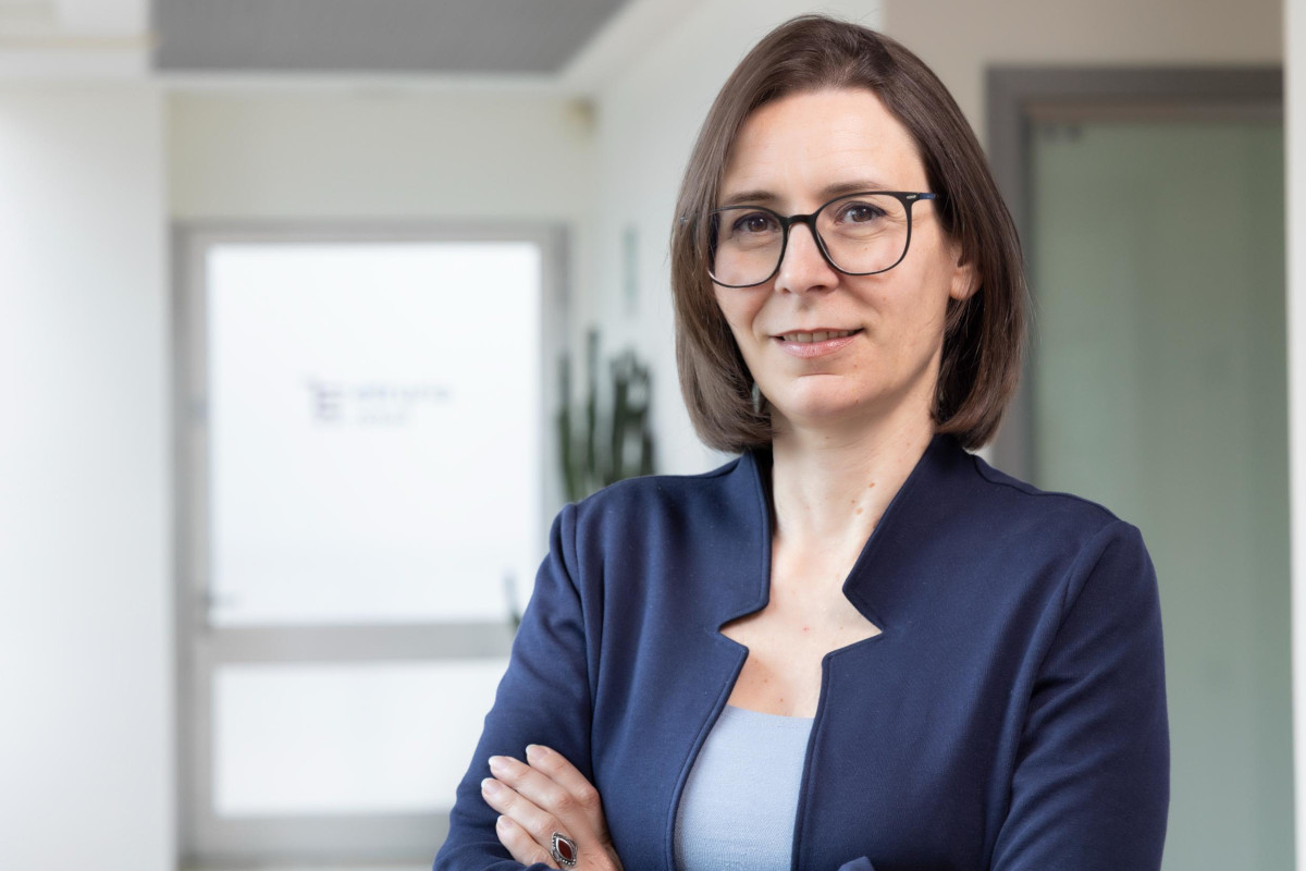 Sara Faucci, nuova manager di Etruria Retail, ritratta in ufficio con giacca blu e occhiali, braccia incrociate.