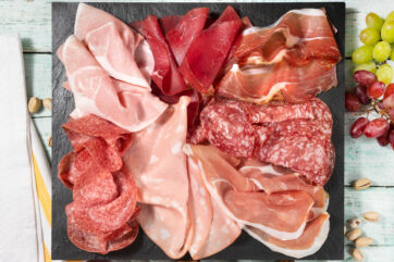 Tagliere di salumi misti con prosciutto, mortadella, salame e bresaola, accompagnato da uva fresca e pistacchi. - Citterio