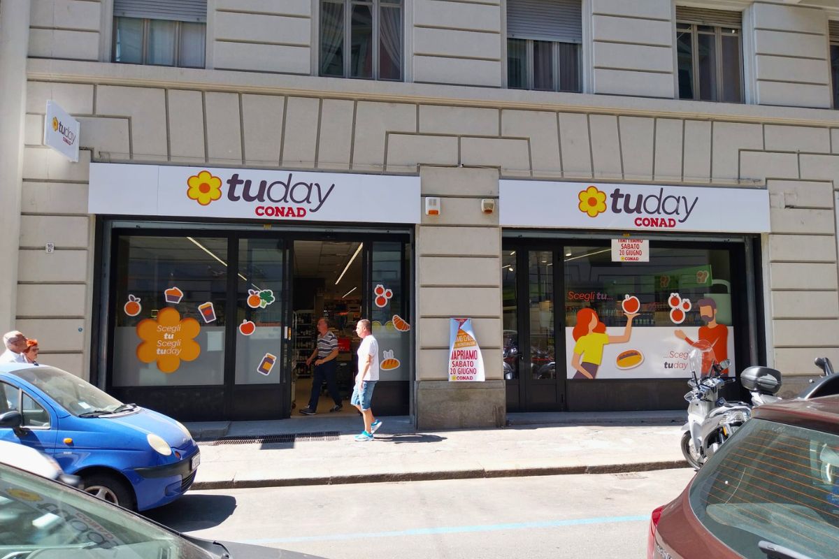 Facciata di un nuovo punto vendita TuDay Conad a Torino con vetrine decorate e insegna luminosa su strada.