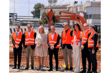 Gruppo di persone in cantiere per la nuova piattaforma logistica Sibeg Coca-Cola a Catania con scavo Hitachi sullo sfondo.