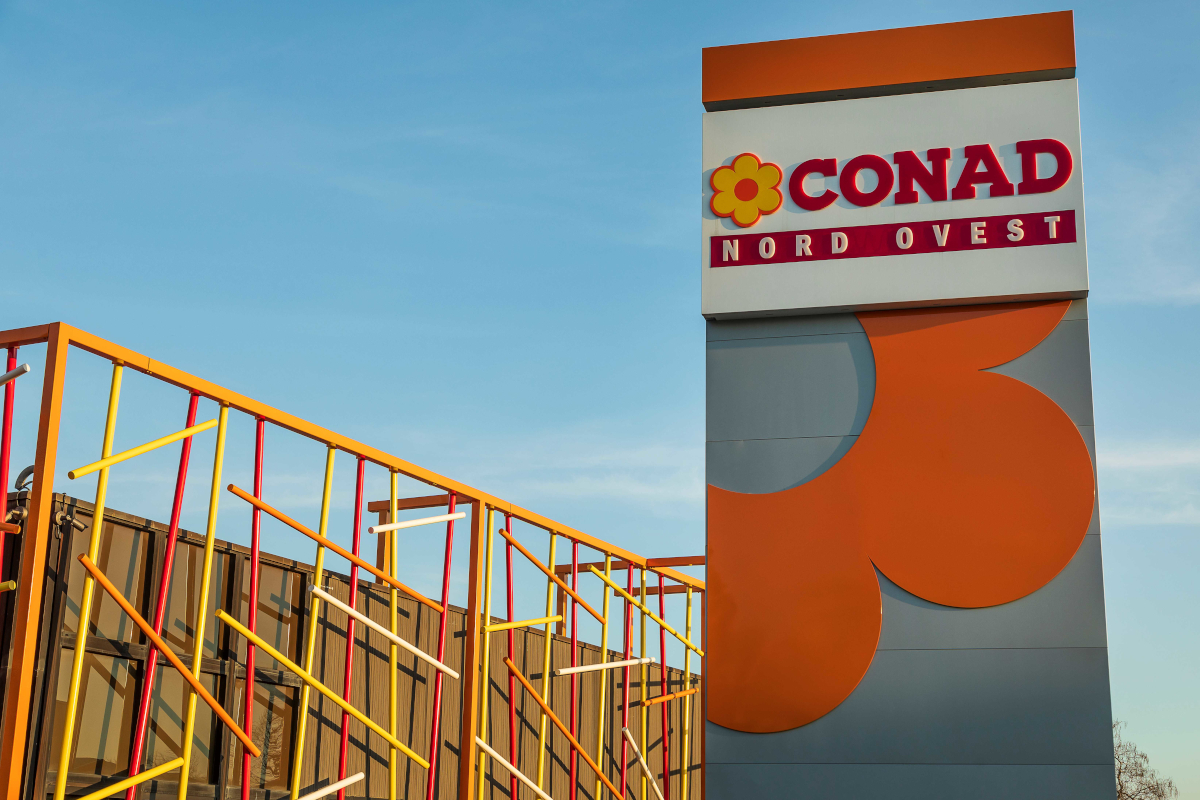 Insegna verticale Conad Nord Ovest presso un punto vendita, simbolo del piano di sviluppo e integrazione Realco.