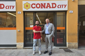 Inaugurazione del nuovo punto vendita Conad City a Modena: due uomini si stringono la mano davanti all'ingresso del negozio.