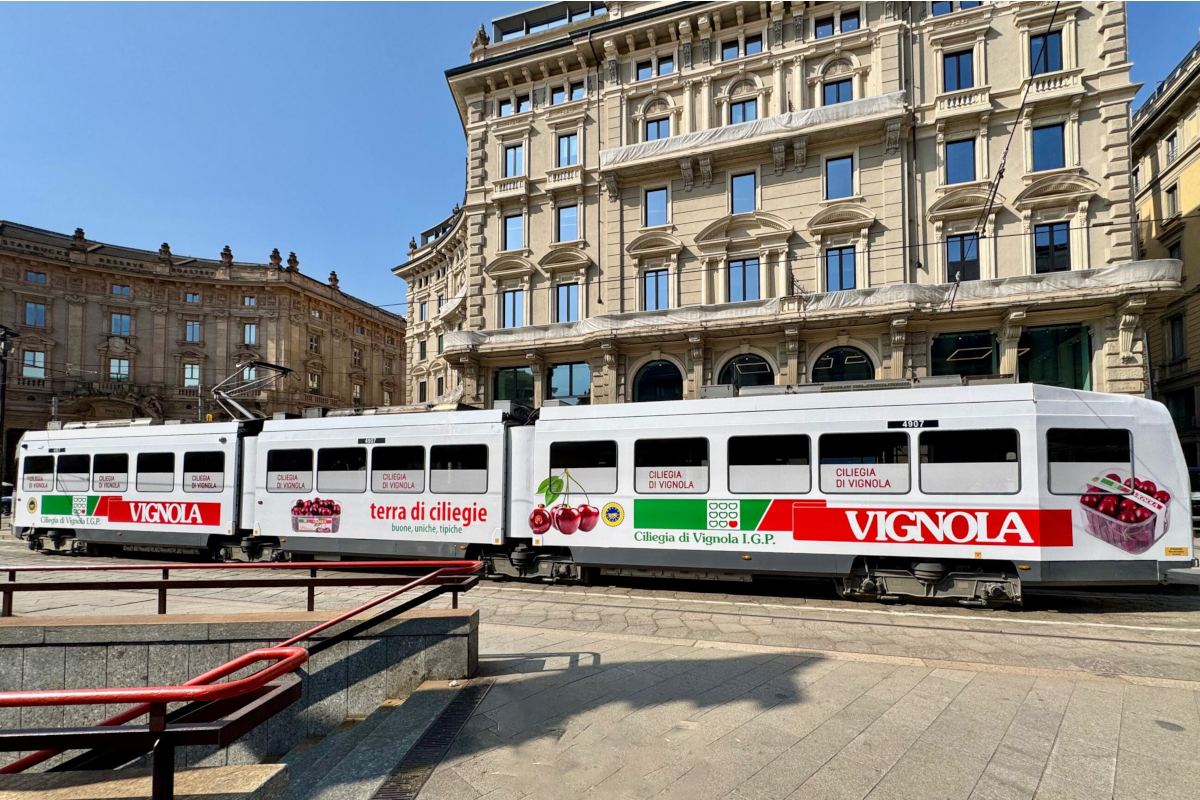 Tram a Milano con pubblicità della Ciliegia di Vignola IGP, eccellenza italiana, in un contesto urbano storico.