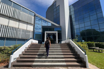 Donna con zaino sale le scale verso l'ingresso di un moderno ufficio aziendale, simbolo di flessibilità oraria e lavoro. - Veronesi