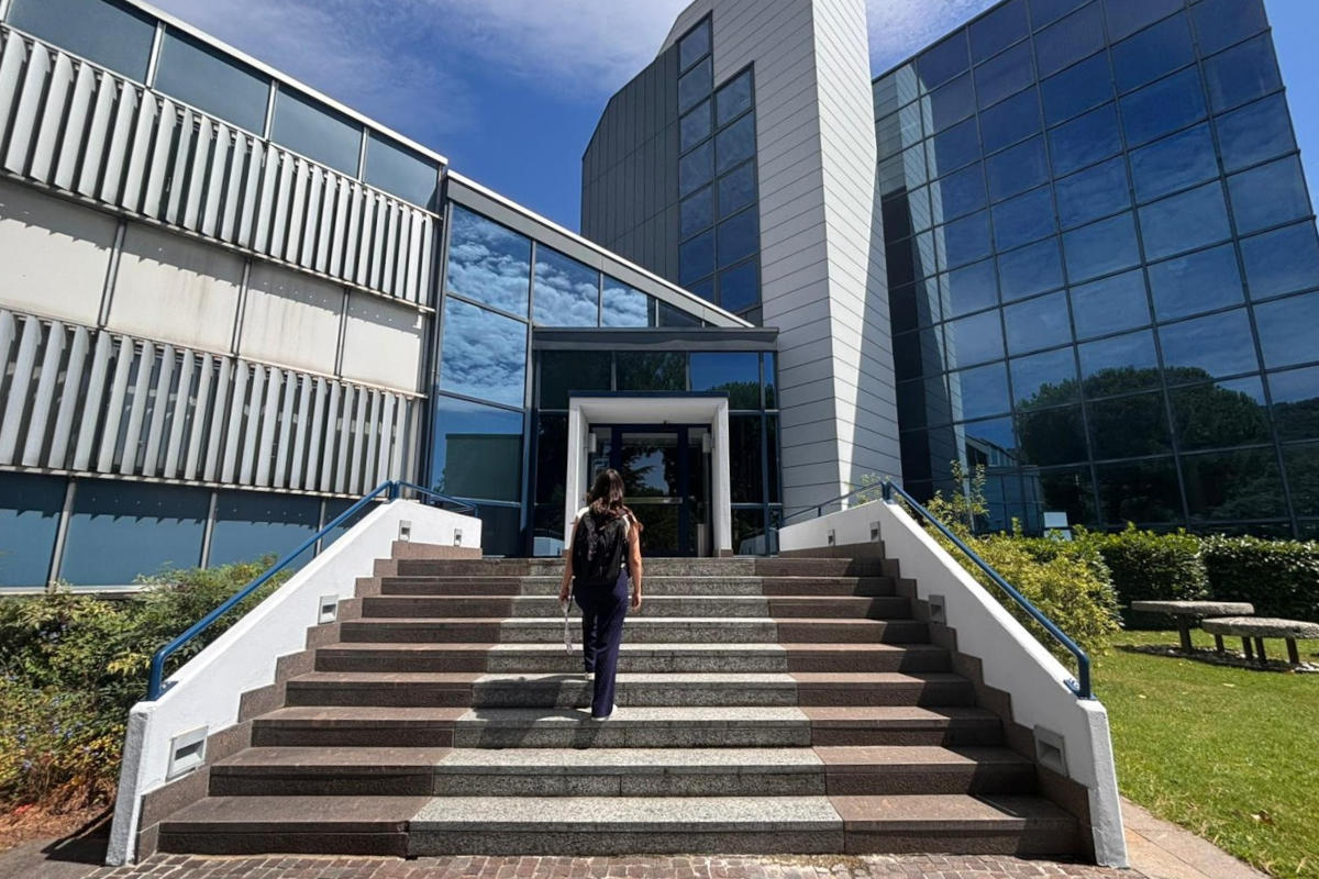 Donna con zaino sale le scale verso l'ingresso di un moderno ufficio aziendale, simbolo di flessibilità oraria e lavoro. - Veronesi