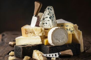 Selezione di formaggi pregiati su tagliere in legno con coltelli professionali, formati pronti all'uso e degustazione.