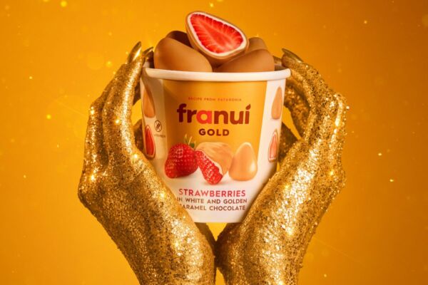 Mani dorate sostengono un barattolo di Franuí Gold, fragole fresche ricoperte di cioccolato bianco e caramello dorato.