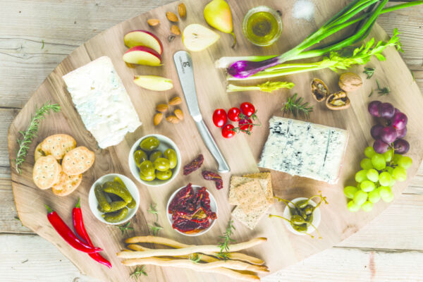 Tagliere di legno con formaggio Gorgonzola, uva, pere, olive, pomodori secchi, cracker, noci e verdure fresche.