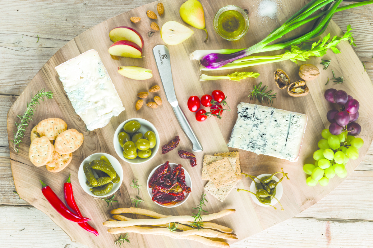 Tagliere di legno con formaggio Gorgonzola, uva, pere, olive, pomodori secchi, cracker, noci e verdure fresche.