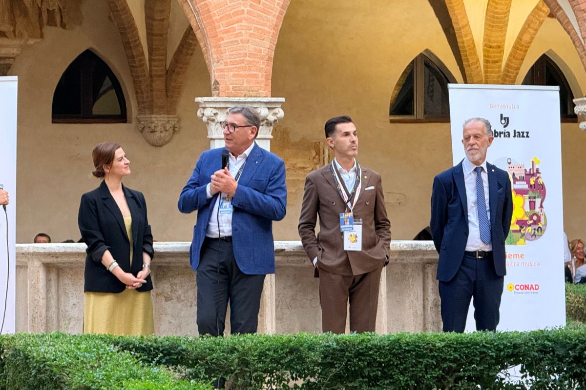 Conferenza stampa Conad e PAC2000A durante Umbria Jazz con relatori davanti a un banner promozionale in un chiostro.