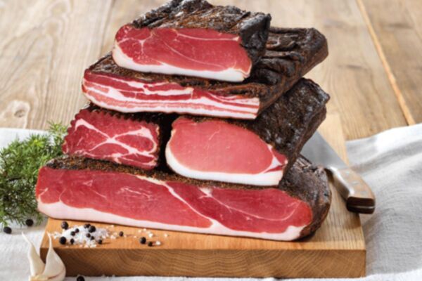 Selezione di tranci di speck e salumi stagionati su tagliere di legno con pepe e sale, per il mercato dei salumi.