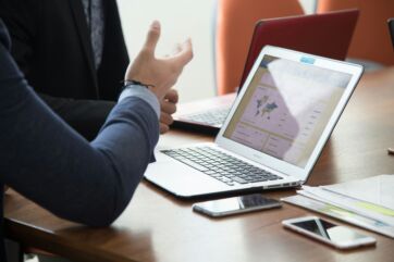 Professionisti in riunione di lavoro discutono davanti a un laptop con grafici e smartphone su un tavolo in ufficio.