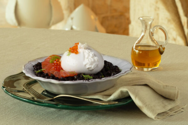 Burrata di Andria Igp servita con salmone, uova di pesce e finocchietto su un letto di legumi scuri e olio extravergine.
