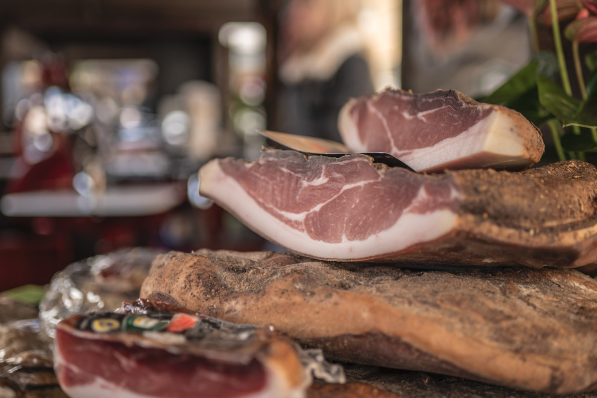 Tranci di Speck Alto Adige IGP in esposizione alla Festa dello Speck, eccellenza gastronomica italiana stagionata.