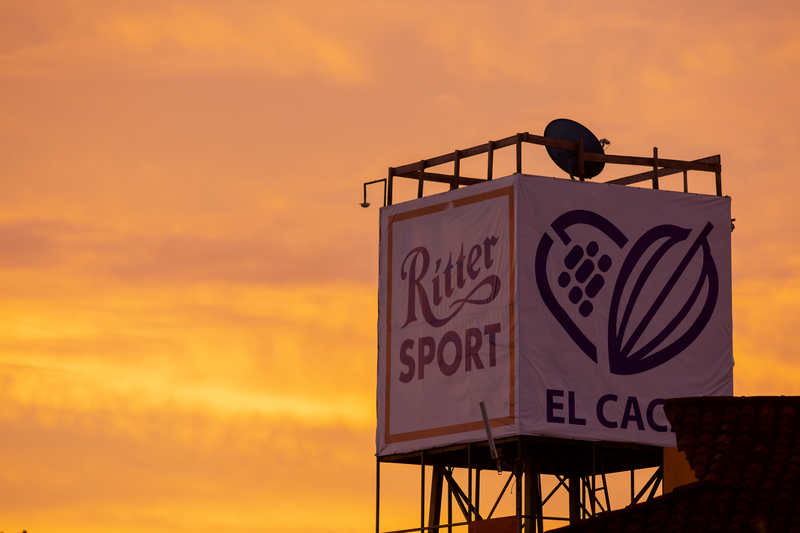 Insegna Ritter Sport e logo El Cacao su impalcatura al tramonto, nuovo fondente