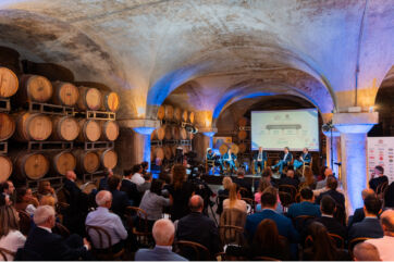 Evento IDGDAY 2026 in cantina con botti di vino, tavola rotonda e pubblico, proiezione L'IA è già qui