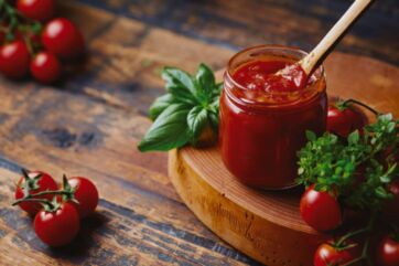 Vaso di conserva di pomodoro artigianale con basilico fresco e pomodorini su tagliere in legno rustico.