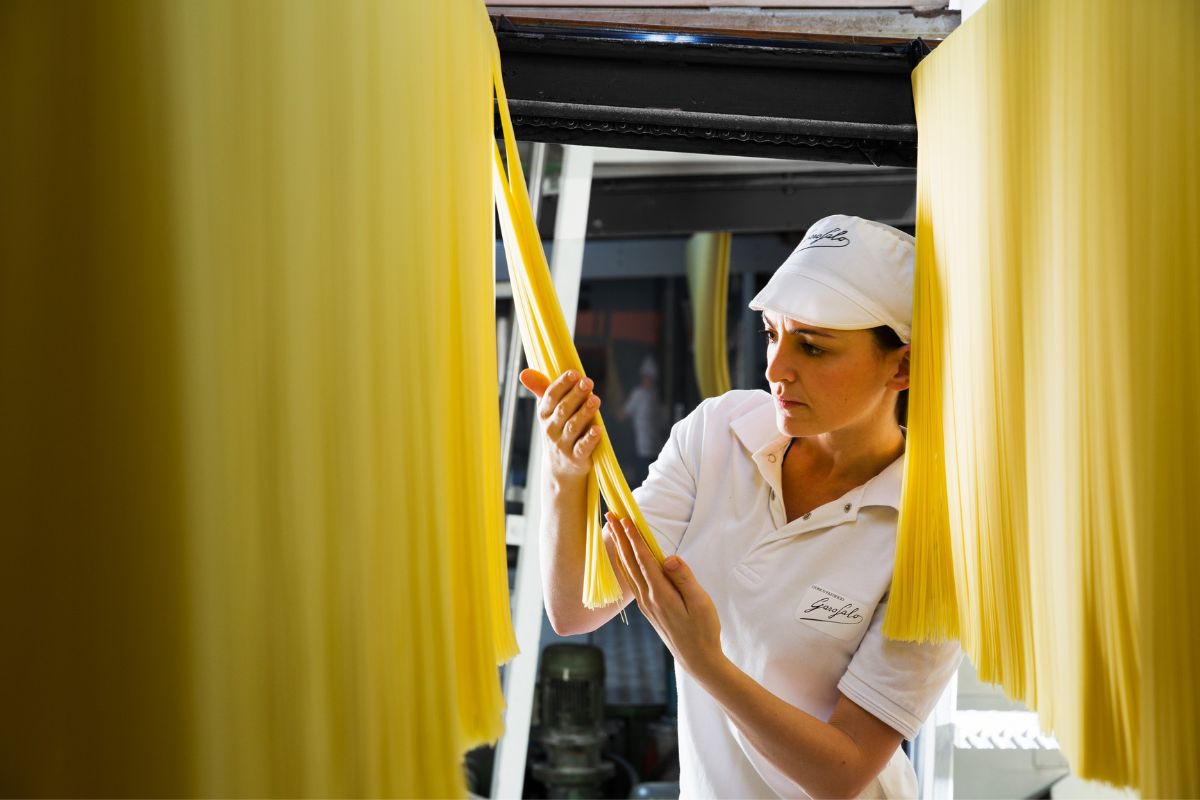 Operaia Garofalo controlla pasta lunga essiccata, simbolo di qualità e tradizione nel pastificio Gragnano