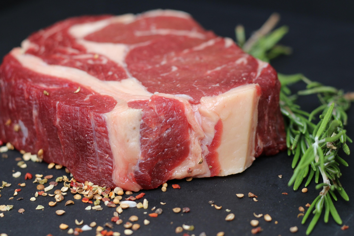 Taglio di carne bovina cruda di alta qualità con rosmarino e spezie su sfondo nero, tema importazione carne UE.