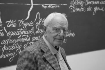 Ritratto in bianco e nero di Alfonso Vitaletti, uomo anziano con occhiali davanti a una lavagna con scritte