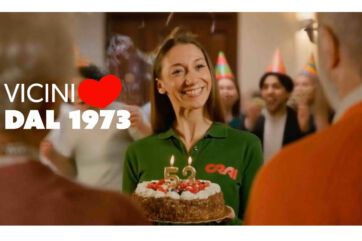 Donna sorridente con maglia verde e torta per i 53 anni Crai in Festa, testo Vicini dal 1973
