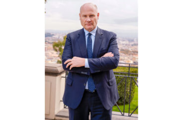 Federico Vecchioni, Presidente Esecutivo BF, in abito blu a braccia conserte con panorama urbano sullo sfondo.
