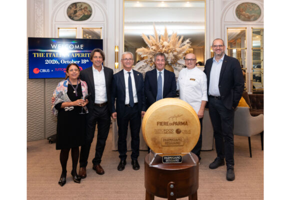Gruppo di sei persone posa con una forma di Parmigiano Reggiano in primo piano, evento Cibus 2024 sold out a sette mesi dall'apertura.