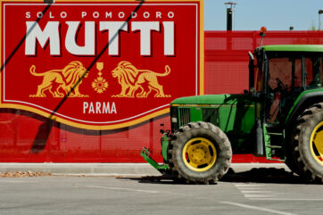 Trattore verde davanti al maxi logo rosso Mutti Parma: campagna pomodoro 2026 e bilancio.