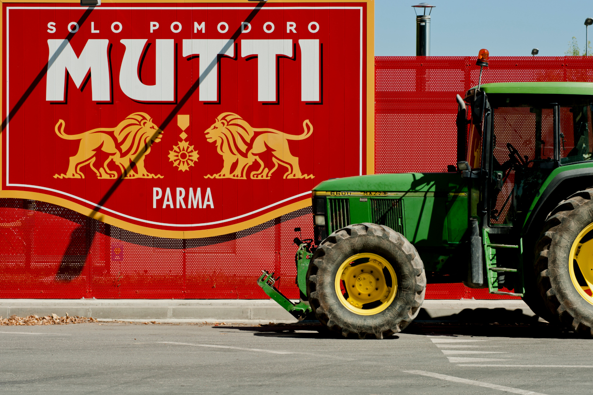 Trattore verde davanti al maxi logo rosso Mutti Parma: campagna pomodoro 2026 e bilancio.