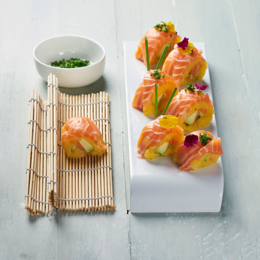 Sushi di salmone norvegese su stuoia di bambù e piatto bianco, con salsa e guarnizioni fresche