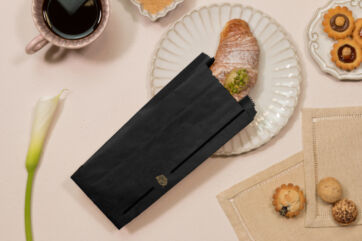 Packaging Esseoquattro nero senza PFAS su tavola con cornetto e caffè, conforme alle norme PPWR