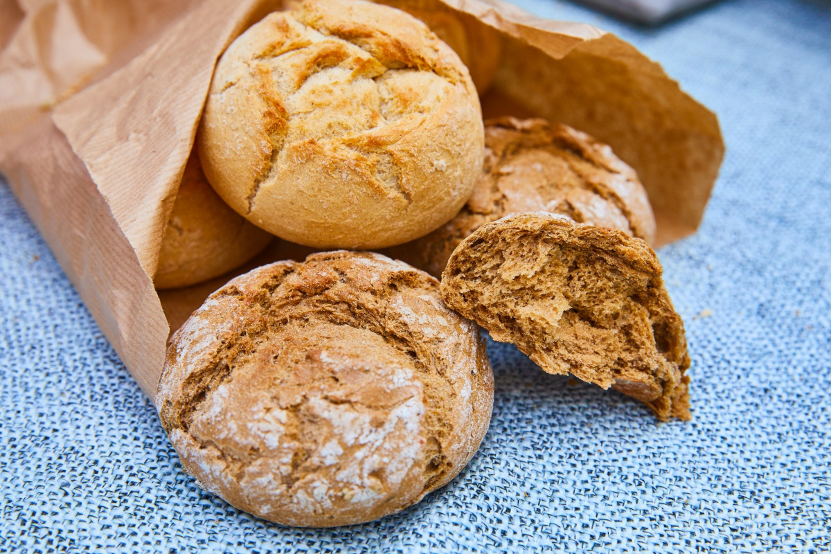 Panini di pane artigianale in sacchetto di carta su canovaccio azzurro, retail pane Italia